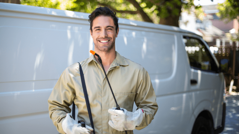 Technicien en lutte antiparasitaire souriant avec un pulvérisateur