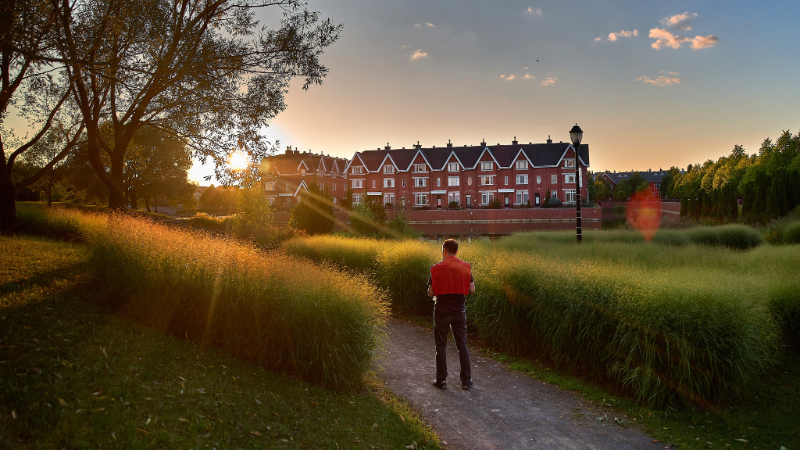 Personne marchant dans un parc au coucher du soleil avec des maisons en arrière-plan